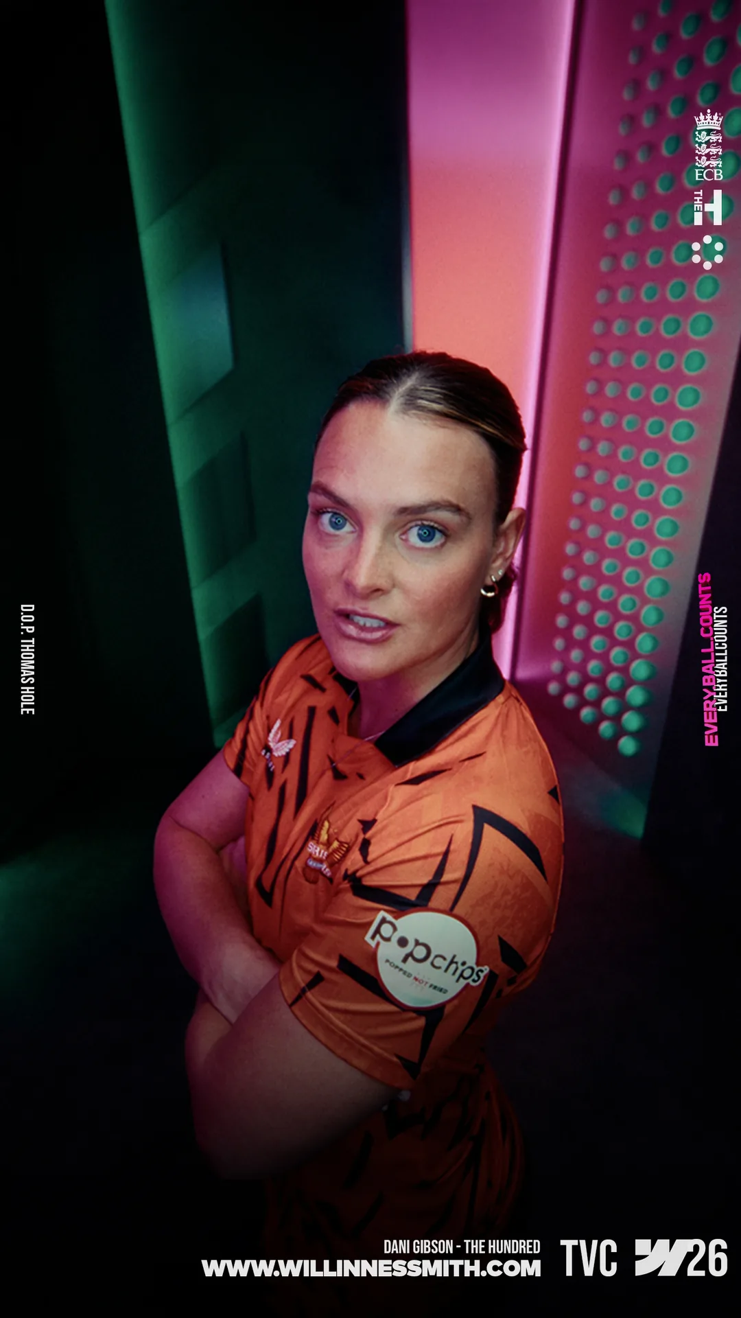 Dani Gibson in an orange shirt between green and pink light panels · The Hundred